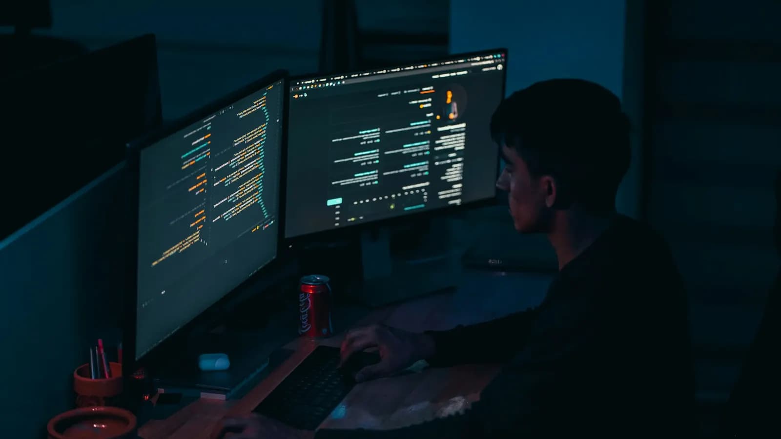 Person working at a laptop and monitors in a dark, blue-lit office