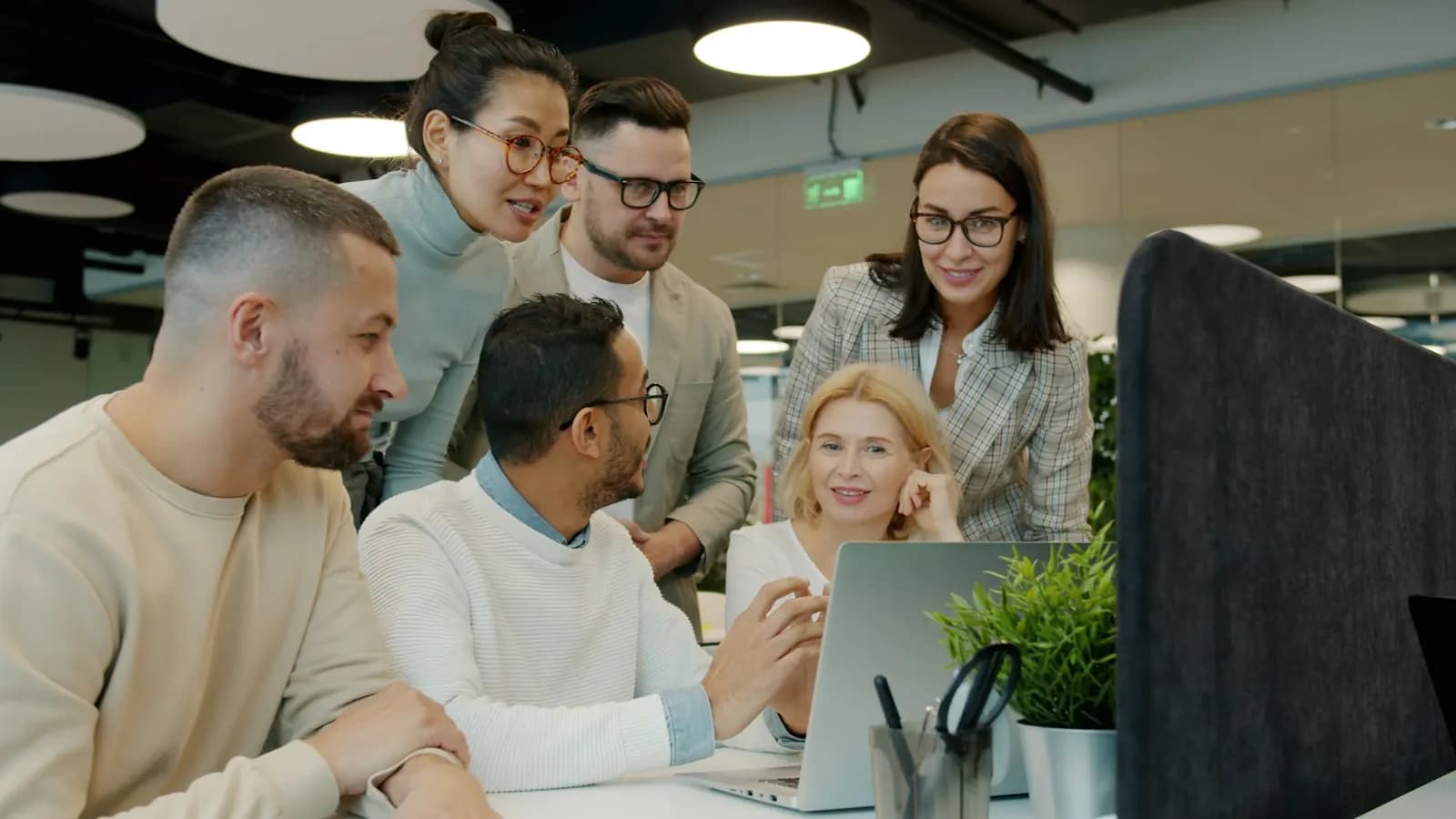 Diverse team gathered around a laptop in a bright open office