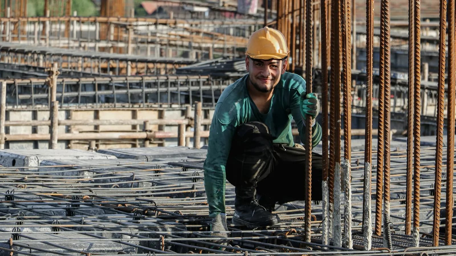 Builder in a yellow hard hat crouching on a construction site