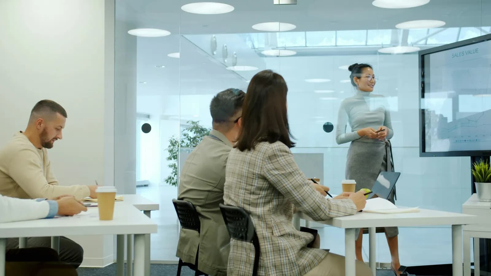 Consultant presenting a sales chart to colleagues in a glass-walled meeting room