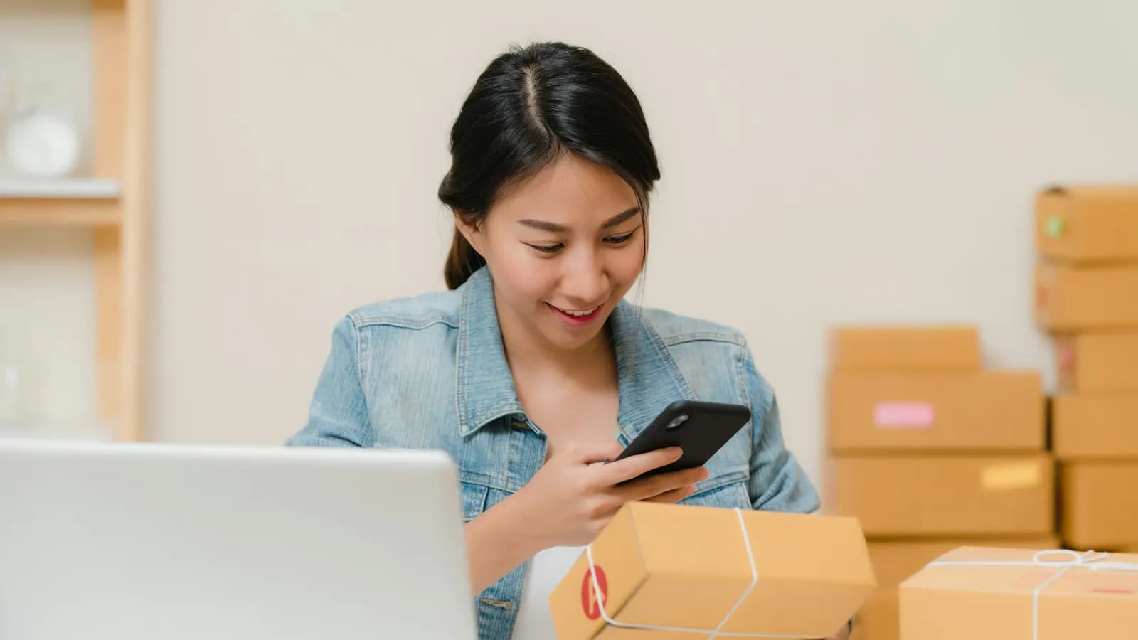 Woman scanning a parcel with her phone beside stacked shipping boxes