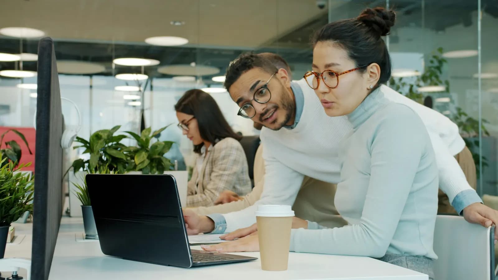 Three colleagues collaborating around a laptop in a meeting room